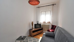 Ein Wohnzimmer mit grauem Sofa, einer Holzeinrichtungsanlage, einem kleinen Tisch und einer Pendelleuchte.
