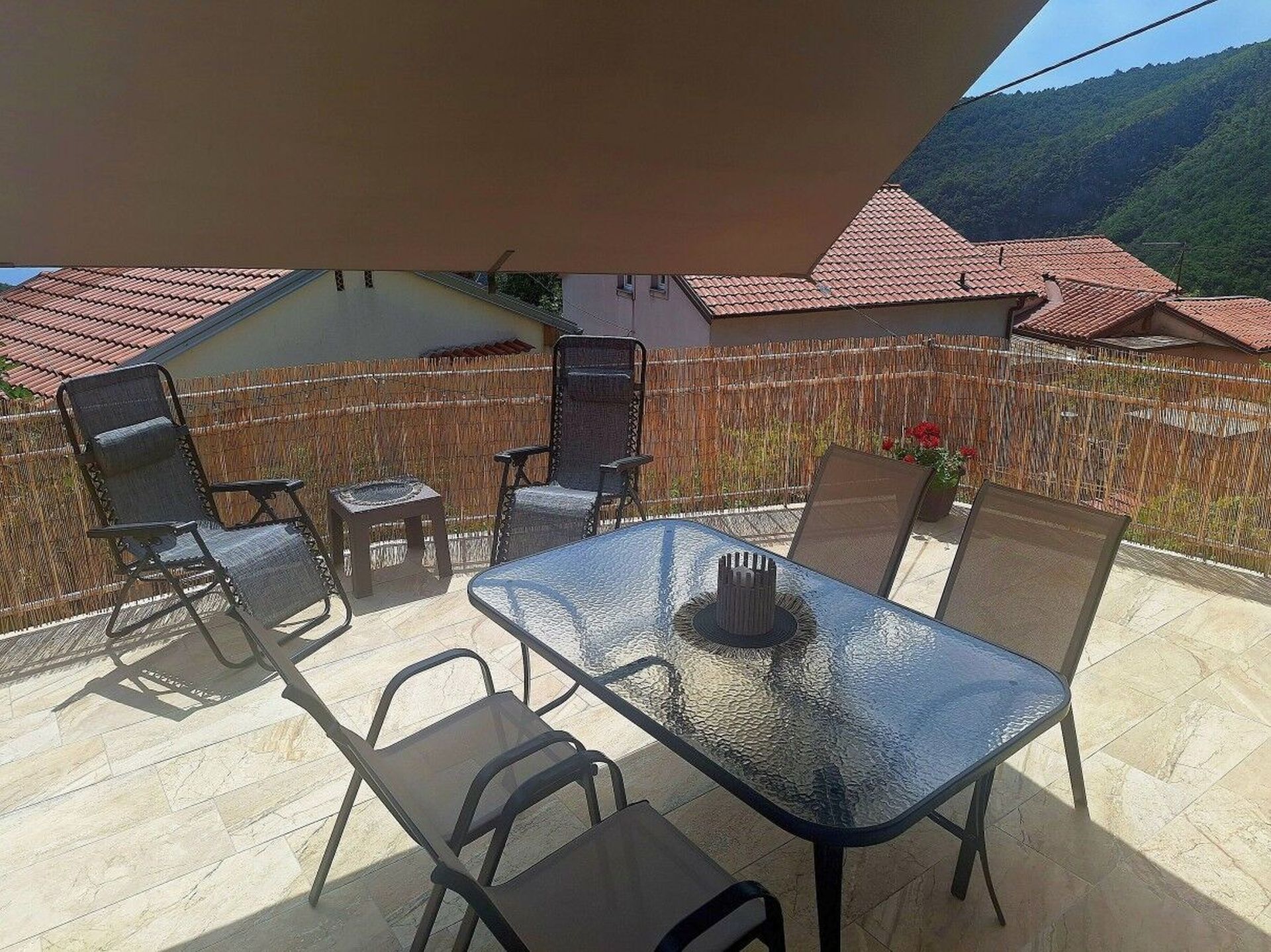 Une terrasse extérieure avec une table et des chaises, une clôture en osier et une chaîne de montagnes en arrière-plan.