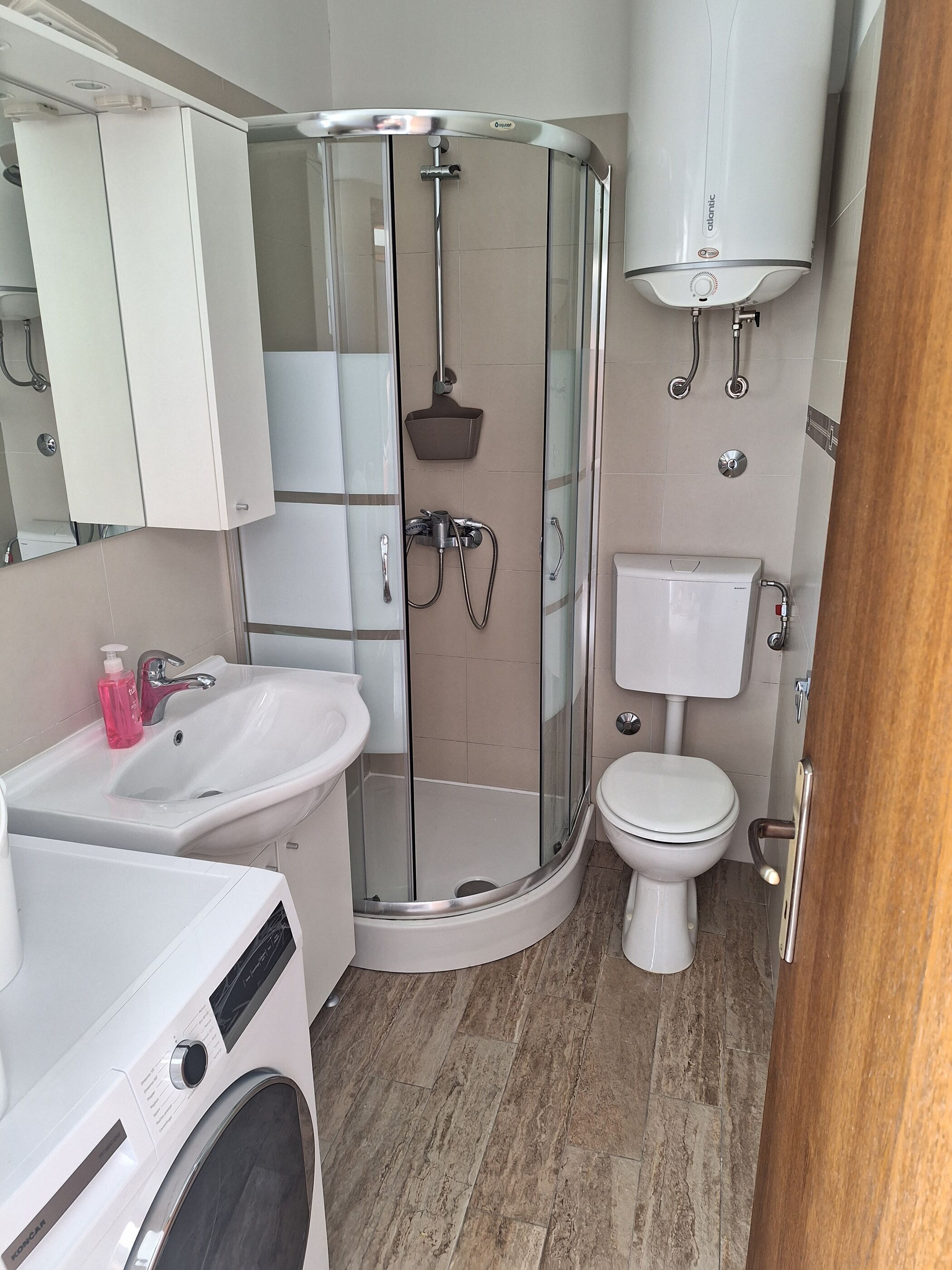 A modern bathroom with a glass-enclosed shower, a sink, a toilet, and a washing machine.