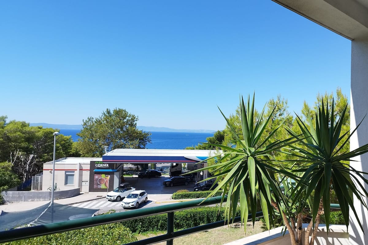 A balcony with a view of a gas station, cars, and the sea.
