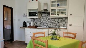 A compact kitchen with white cabinets, a microwave, and a tiled backsplash. - Apartment Orlic (Senj)