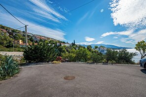 A paved area with a manhole cover, surrounded by greenery and overlooking a body of water with mountains in the distance. - Apartment Orlic (Senj)