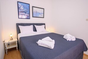A neatly made bed with a dark blue quilt, two white pillows, and two rolled towels on the bed. - Apartment Orlic (Senj)