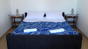 A single bed with a blue and white patterned bedspread, two bedside tables with lamps, and a painting on the wall. - Apartment Orlic (Senj)
