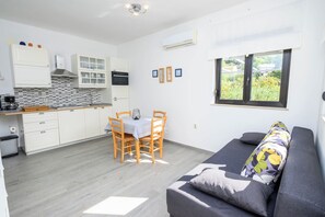 Eine kleine Küche mit weißen Schränken, ein Essbereich mit Tisch und Stühlen sowie ein Sofa mit gemustertem Kissen.