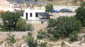 A building with a stone facade, a balcony, and a view of a rocky hillside. - Apartment Orlic (Senj)