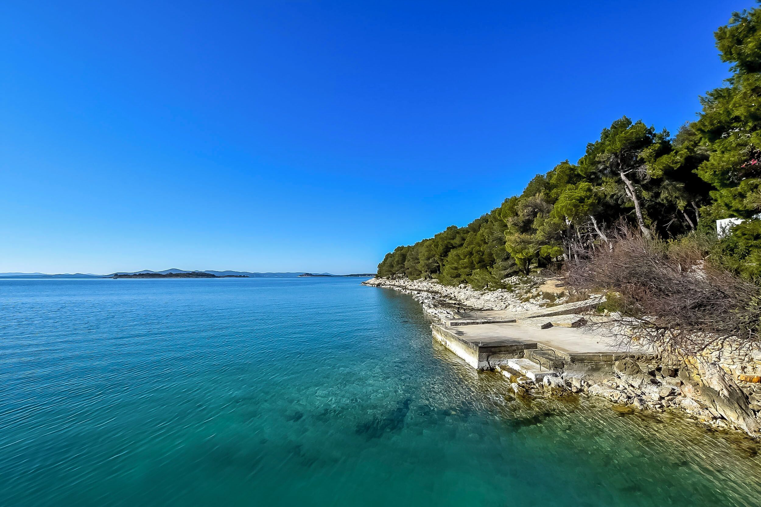 A coastal scene with clear blue water, rocky shoreline, and a pier.