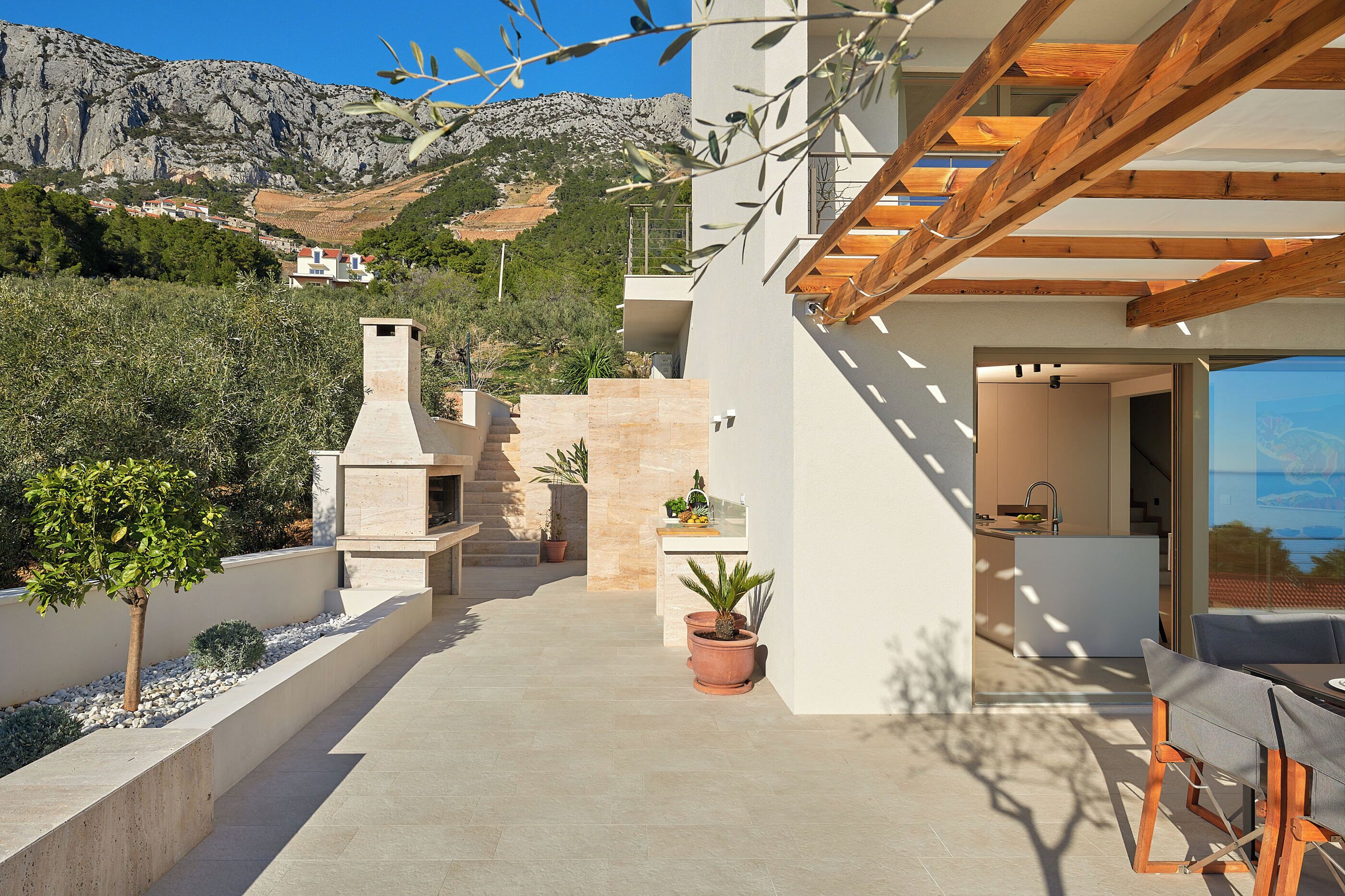 Une maison moderne avec une cheminée en pierre, des plantes en pot et une vue sur un paysage montagneux.