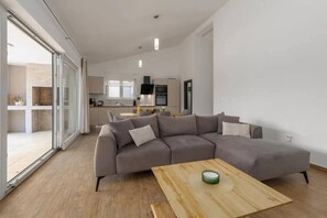 Un soggiorno moderno con un divano modulare grigio, un tavolino in legno e una porta scorrevole in vetro che dà su un balcone.