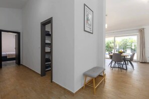 A room with a wooden floor, a bench, a dining table with chairs, and a view of the outdoors through large windows. - Villa Deluxe (Rasa)