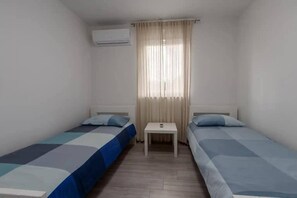 A small, clean room with two single beds, a small table, and an air conditioning unit. - Villa Deluxe (Rasa)