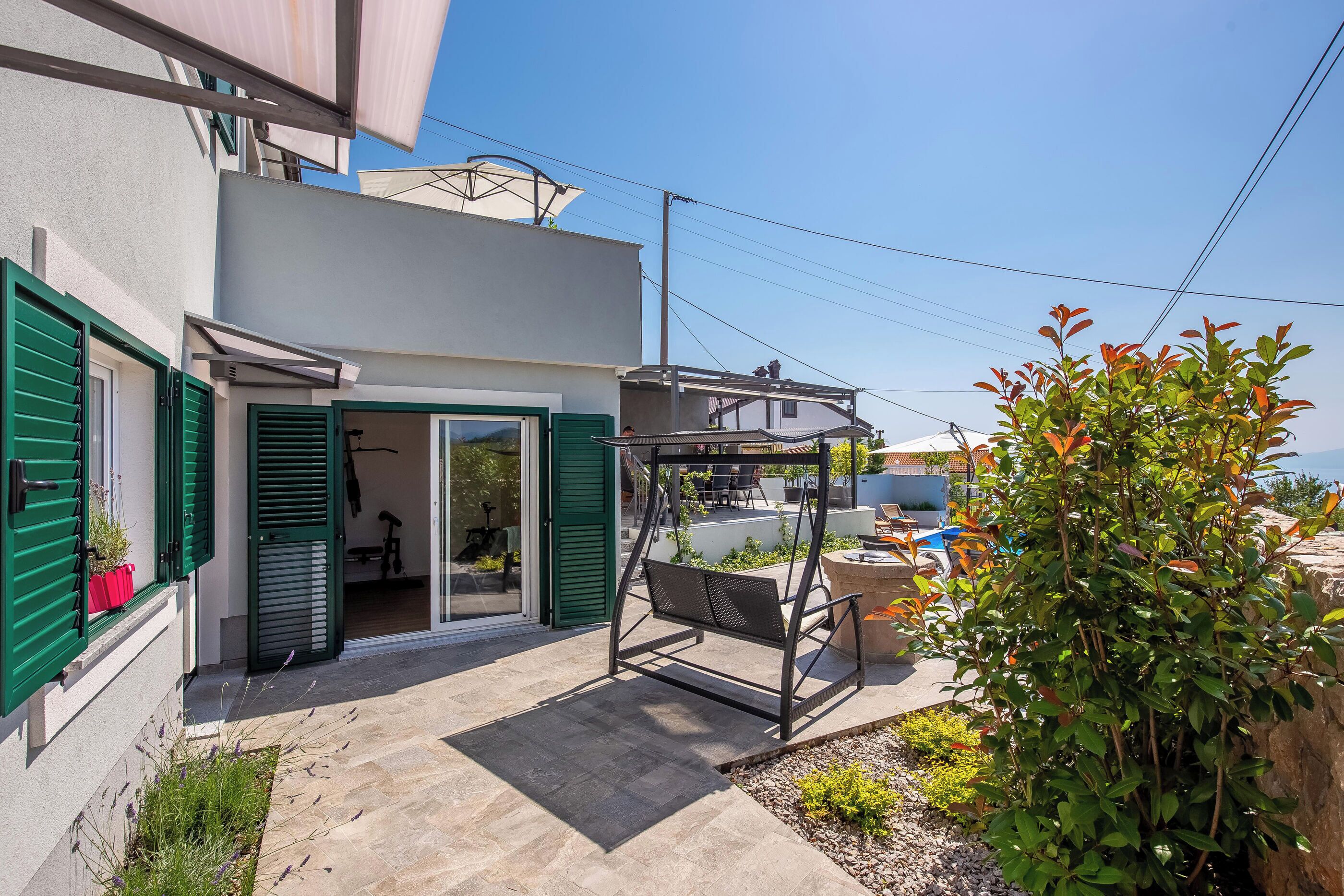 Une maison moderne dotée d’un patio, de volets verts et d’une chaise suspendue.