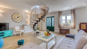 Ein modernes Wohnzimmer mit Wendeltreppe, einer großen Wanduhr, einem Fernseher, einem Sofa und einem Couchtisch mit Obst.
