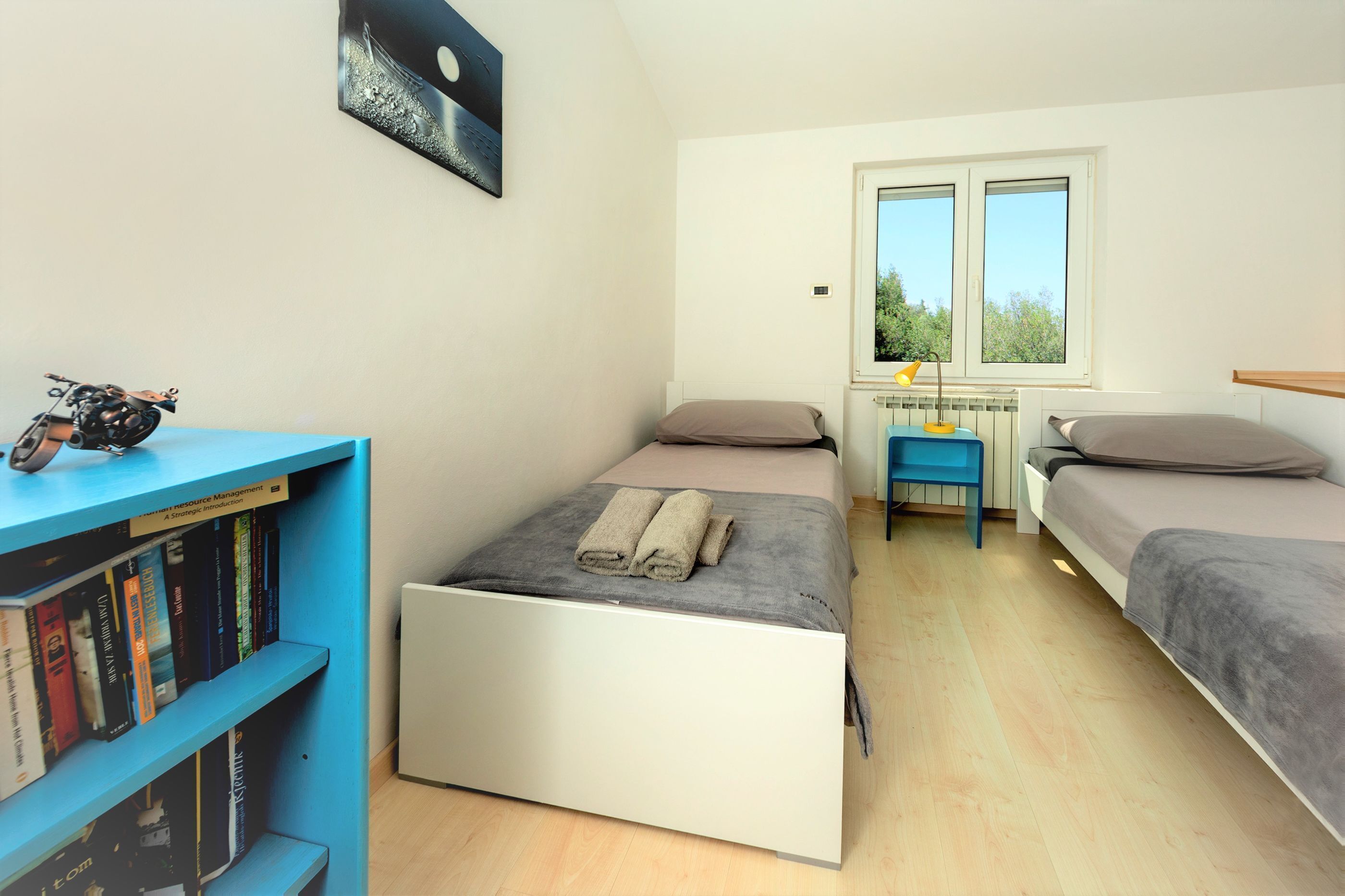 A bedroom with a single bed, a small desk, a bookshelf, and a window with a view.