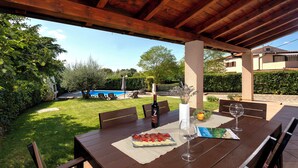 Une terrasse extérieure avec une table en bois dressée pour le dîner, une bouteille de vin et un verre posés sur la table.