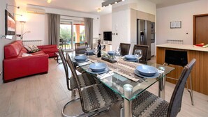 Un salon moderne avec un canapé rouge, une table à manger en verre pour quatre personnes et un coin cuisine équipé d’un réfrigérateur et d’une cuisinière.