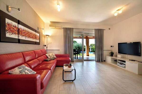 A modern living room with a red leather sofa, a coffee table, a flat-screen TV, and a large window with curtains. - Villa Nina (Porec)