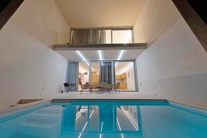 Ein moderner, überdachter Innenpool, ein Essbereich mit Stühlen und eine durch Glastüren einsehbare Küche.