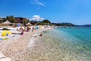Una playa con aguas transparentes y poco profundas, sombrillas y gente relajándose.