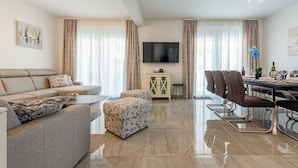 Una sala de estar moderna con sofá, otomanas, mesa de comedor, sillas y televisor.