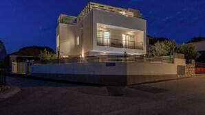 Una casa moderna de dos pisos con balcón, entrada con reja y un muro de piedra.