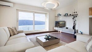 A modern living room with a sofa, coffee table, and a TV on a white stand. - Villa Royal Blue (Rasa)