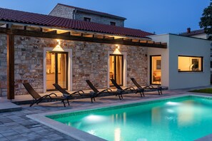 Une maison moderne avec une façade en pierre, une piscine et des chaises longues.