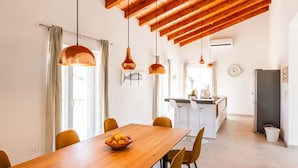 Une cuisine moderne dotée d’un îlot central, de luminaires suspendus et d’un coin repas avec une table et des chaises en bois.