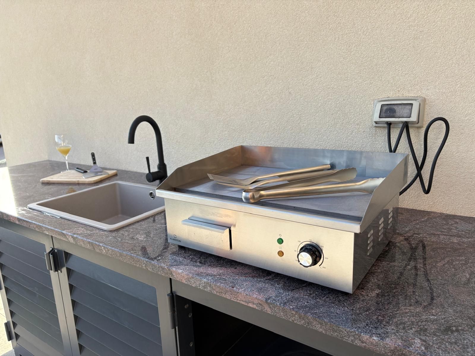 Cocina exterior compacta con pileta, parrilla integrada y panel de control.
