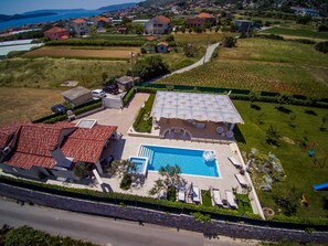 An aerial view of a residential property with a swimming pool, multiple houses, and a road. - Villa Malo (Seget)