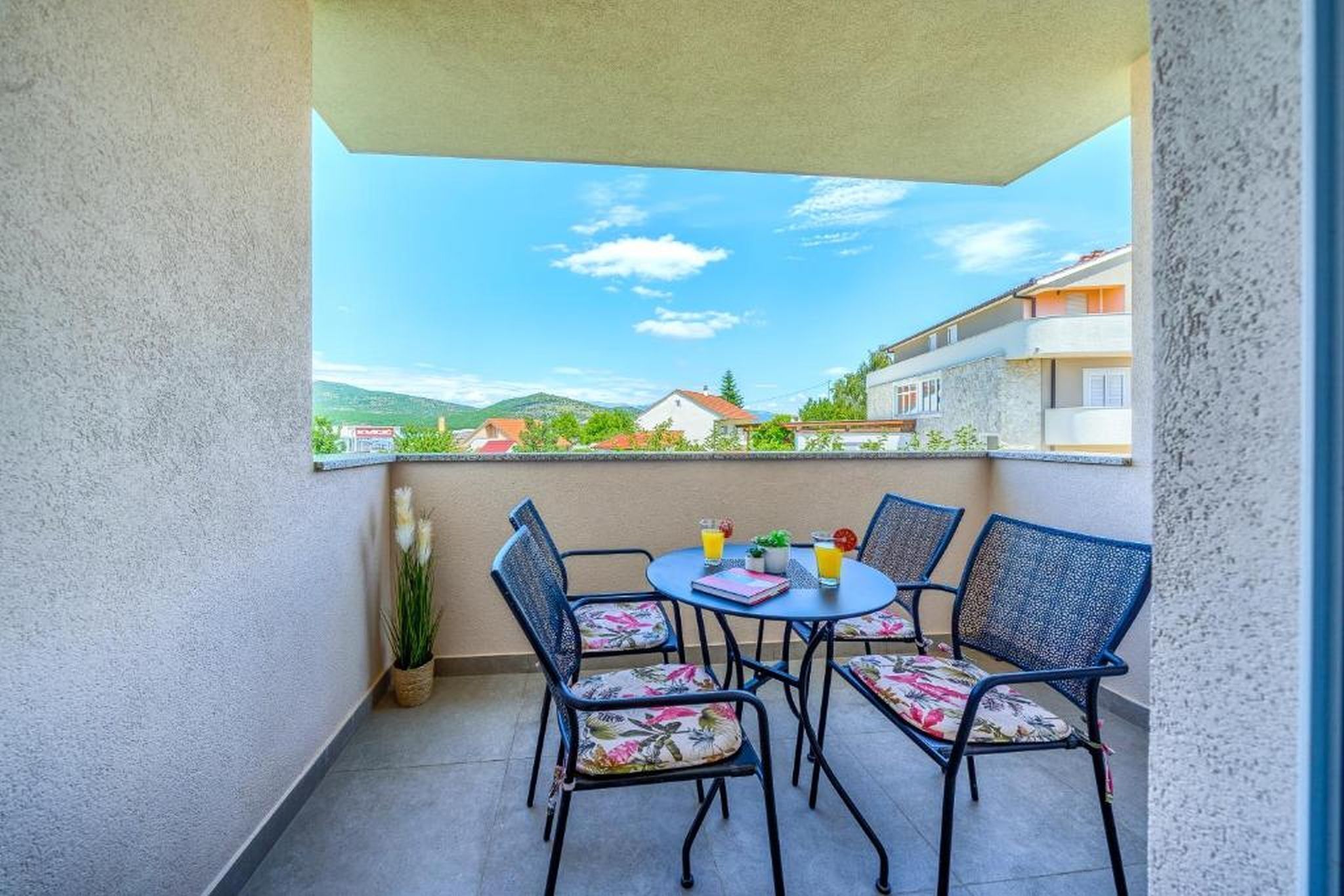 Een balkon met een tafel en stoelen, uitzicht op gebouwen en heuvels, en een heldere lucht.