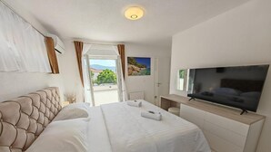 A modern bedroom with a large bed, a TV, and a view of the outdoors. - Villa Nikoma (Dicmo)