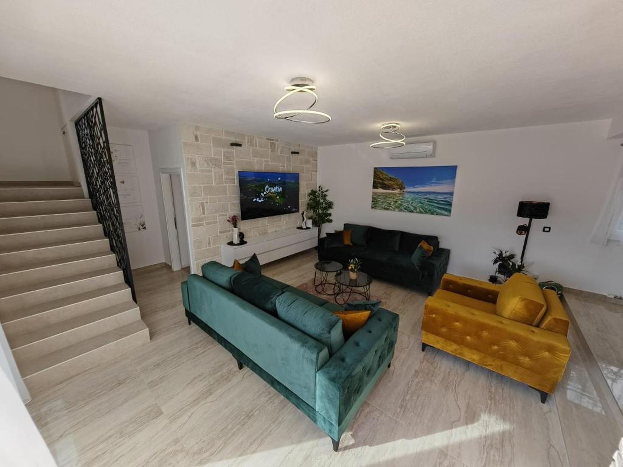 A modern living room with a staircase, a flat-screen TV, a sofa, a yellow armchair, and a coffee table.