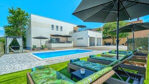 A modern outdoor pool area with lounge chairs and umbrellas. - Villa Nikoma (Dicmo)