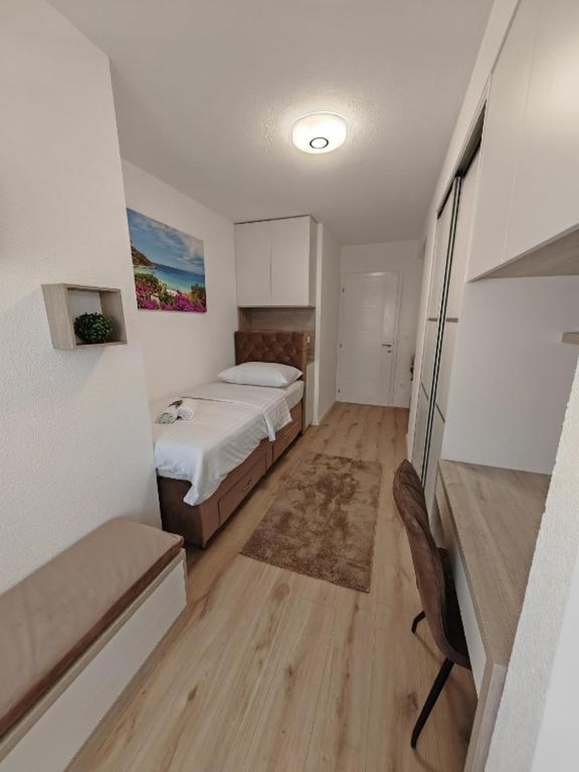 Una stanza piccola e funzionale con un letto, una scrivania, una sedia e un quadro appeso al muro.