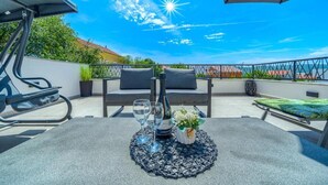 A rooftop terrace with a table set for two, featuring a bottle of wine, glasses, and a small vase with flowers. - Villa Nikoma (Dicmo)