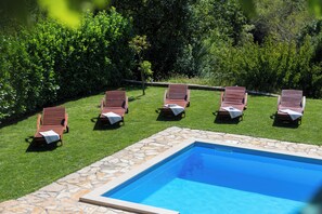 A swimming pool with six wooden lounge chairs arranged around it, set in a lush green garden. - Villa Green Oasis (Proložac)