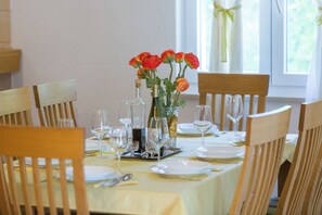 A dining table set with white plates, cutlery, and wine glasses, surrounded by wooden chairs. - Villa Green Oasis (Proložac)