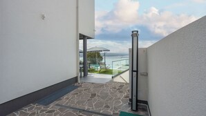 A stone-tiled outdoor area with a glass balustrade overlooking a body of water. - Villa Eva (Crikvenica)