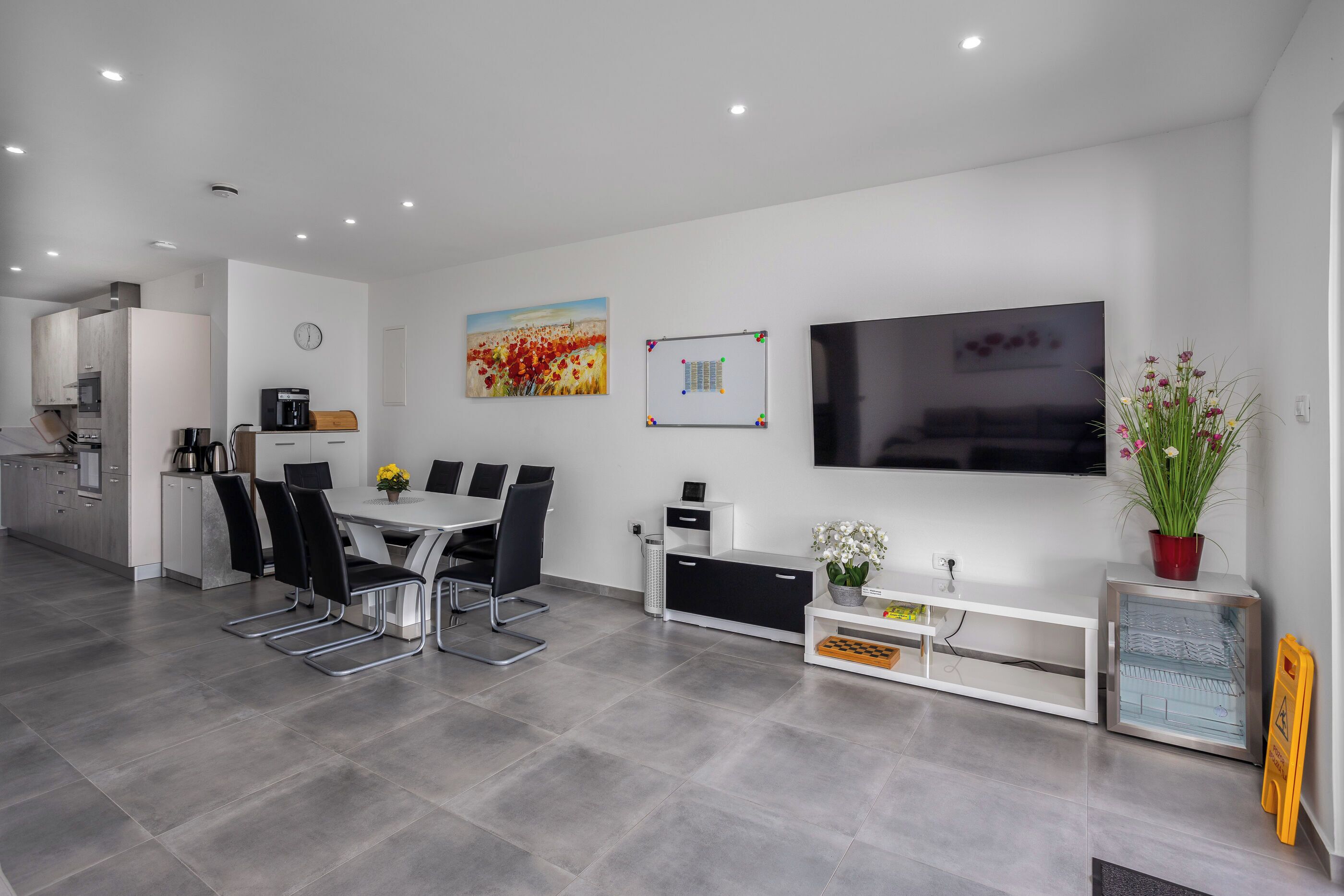 A modern kitchen with a dining area, a flat-screen TV, and a potted plant.