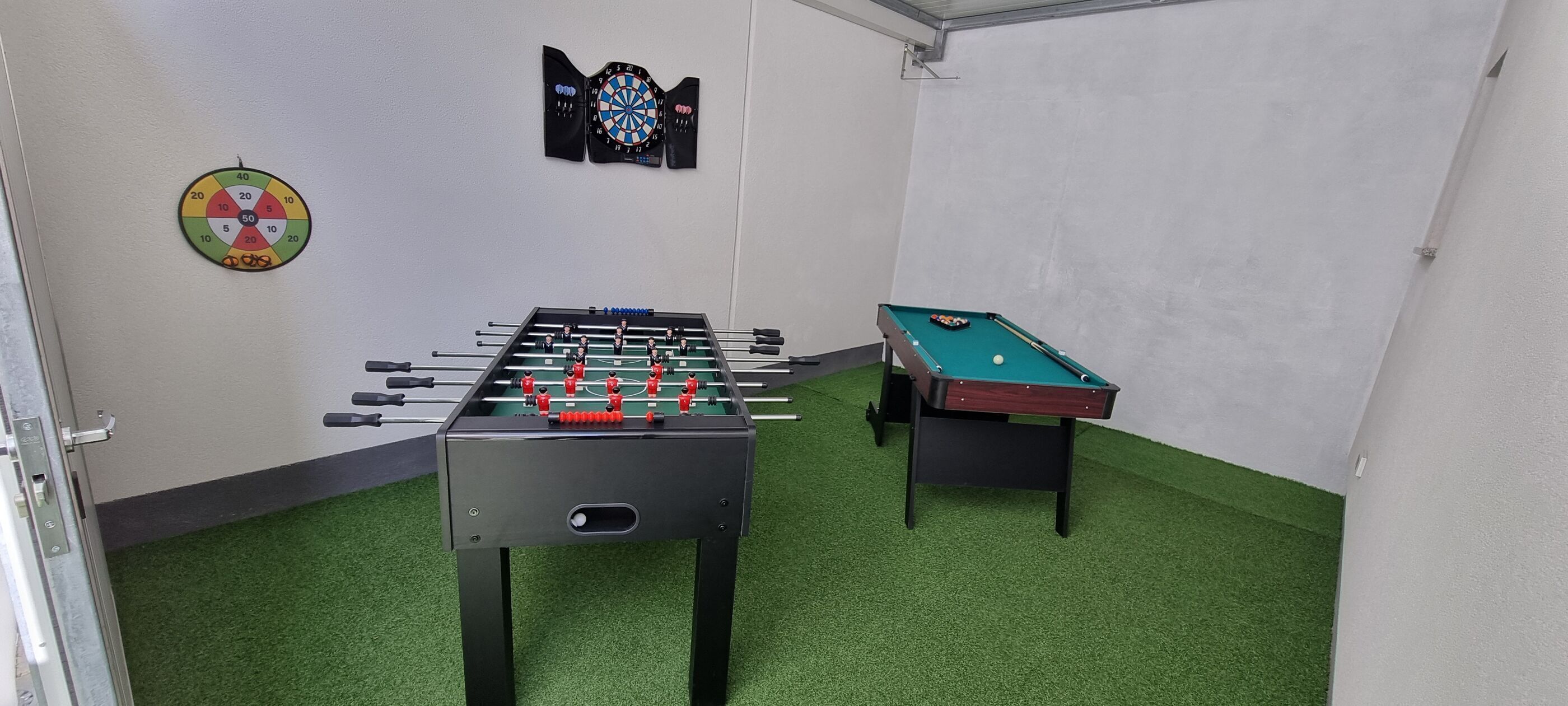 Une pièce équipée d’un baby-foot, d’une table de billard et de deux cibles de fléchettes fixées aux murs.