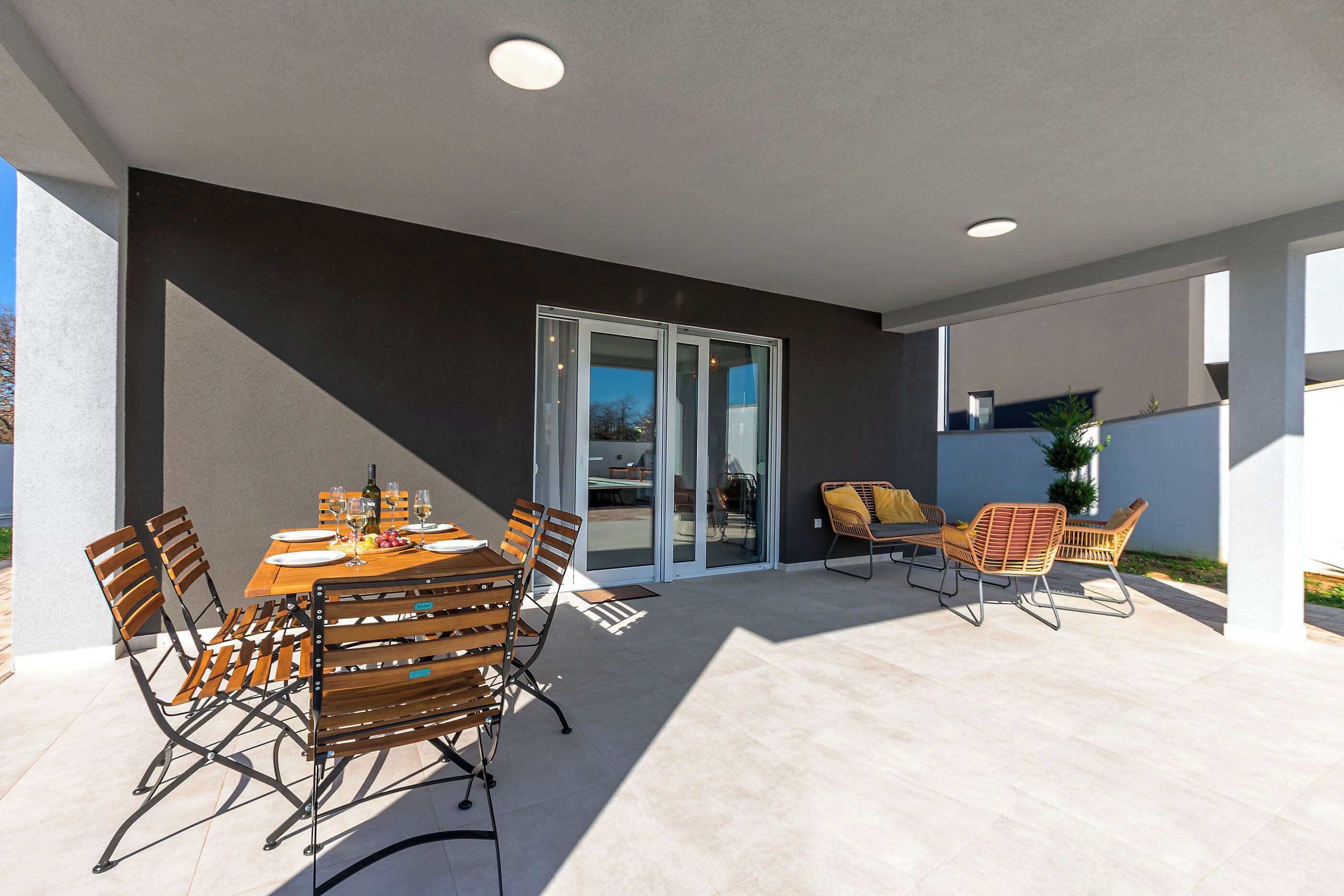 An outdoor patio with a table set for dining, surrounded by chairs, and a sliding glass door leading to an interior space.