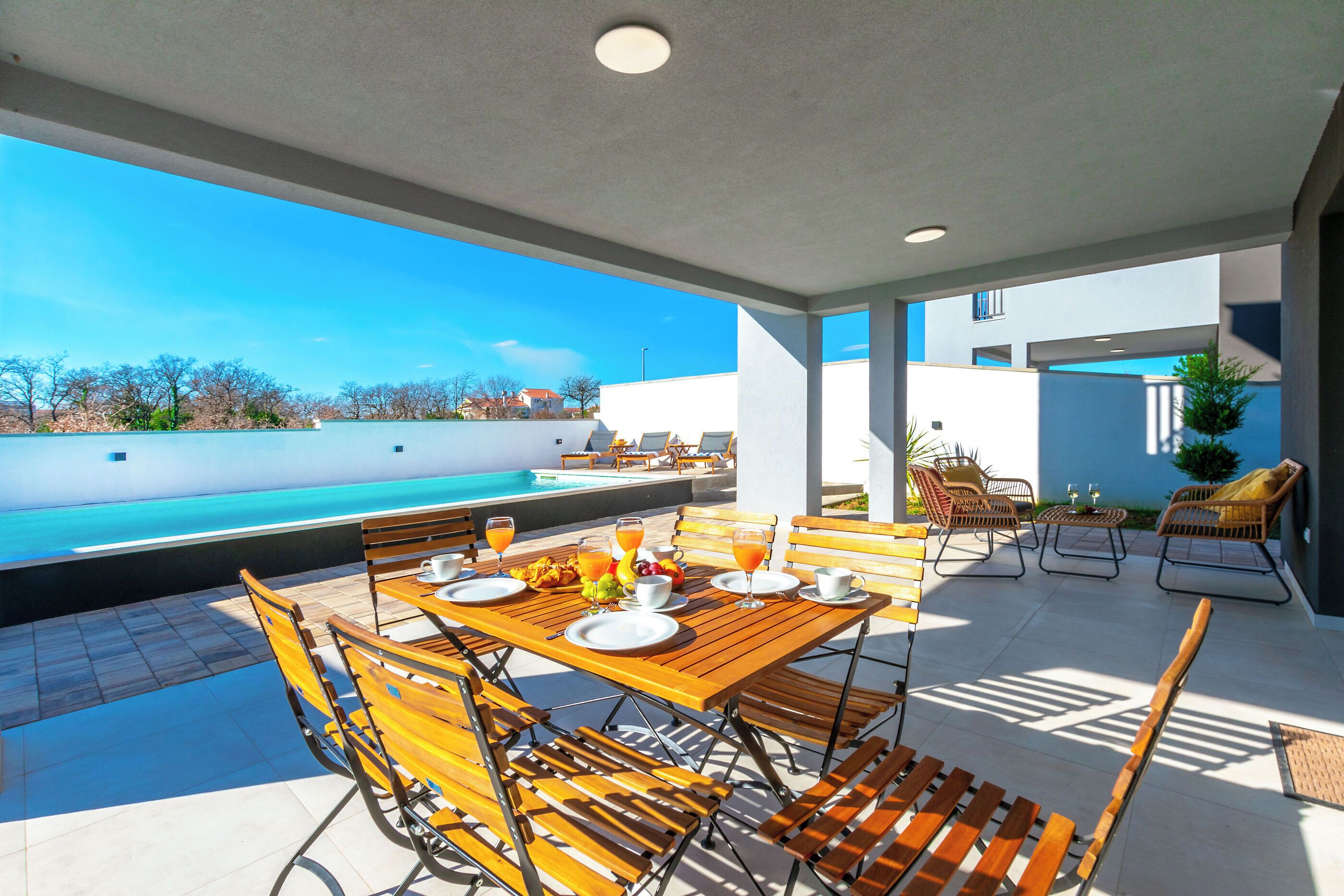 Un espace de restauration en plein air avec vue sur la piscine, doté de mobilier en bois et offrant un ciel dégagé.
