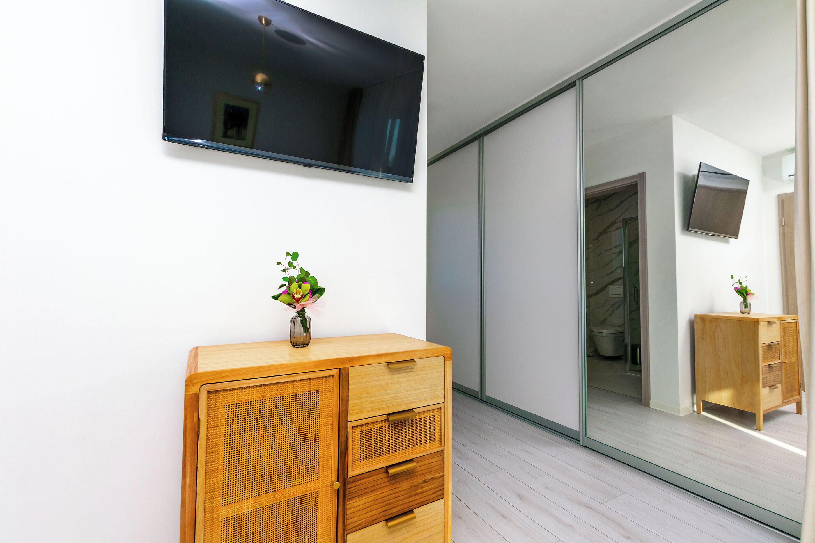 A modern room with a wooden cabinet, a flat-screen TV mounted on the wall, and a sliding glass door leading to a bathroom.