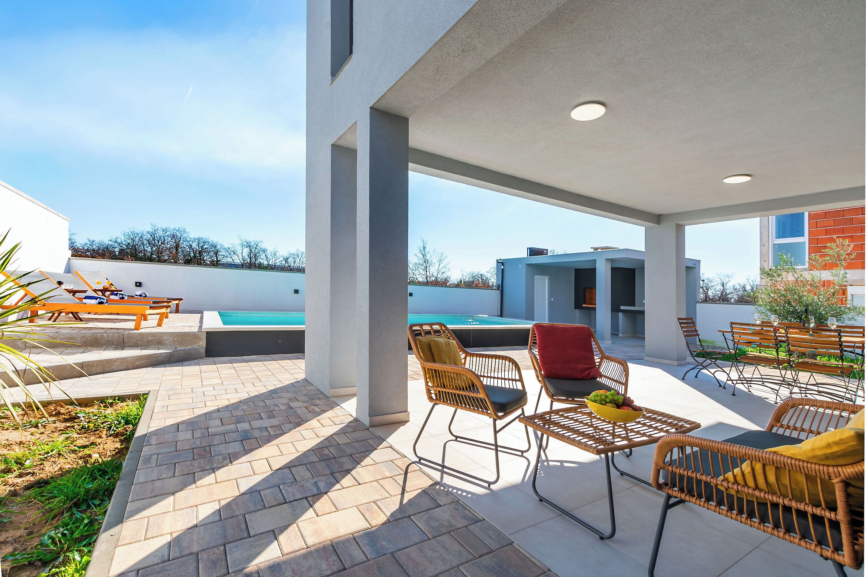 Un patio al aire libre con mobiliario de mimbre, una piscina y vistas a un edificio moderno.