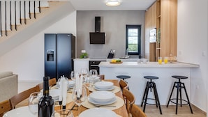 A modern kitchen with a central island, built-in appliances, and a dining area with a wooden table and chairs. - Villa A Lauda (Pakostane)