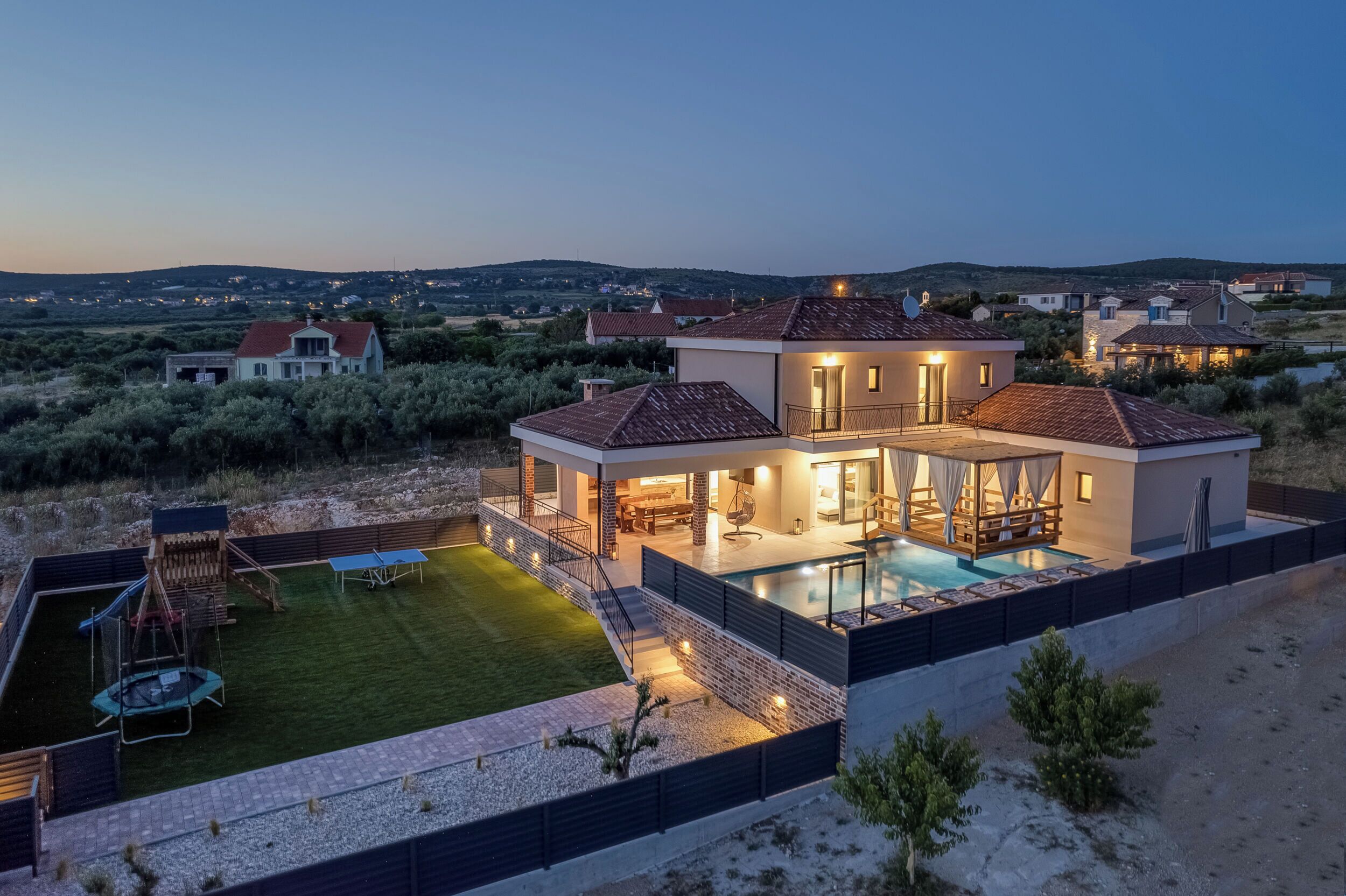 Ett modernt hus med en swimmingpool, en täckt uteplats och en välskött gräsmatta.