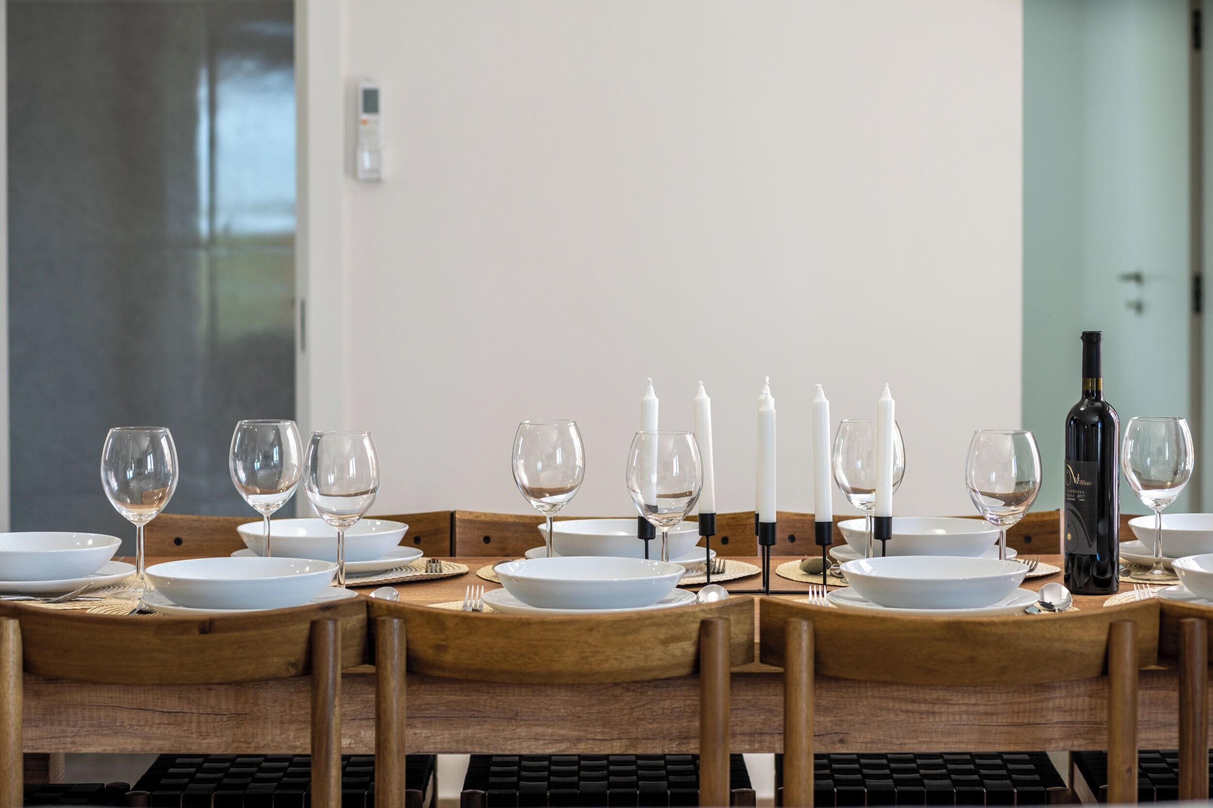 Une table à manger dressée avec de l’argenterie blanche, des verres à vin et des bougies, et une bouteille de vin placée à droite.