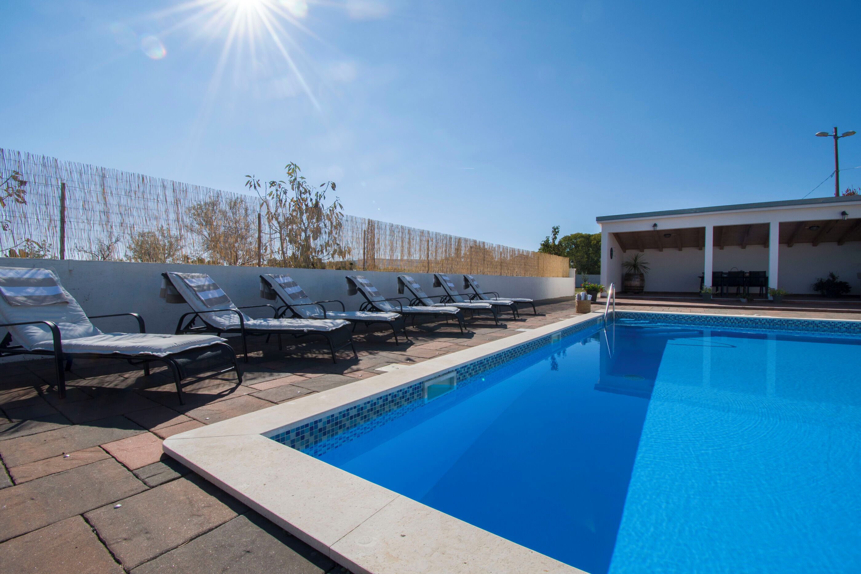 A swimming pool with lounge chairs and a covered area.