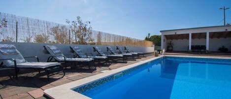 A swimming pool with lounge chairs and a covered area.